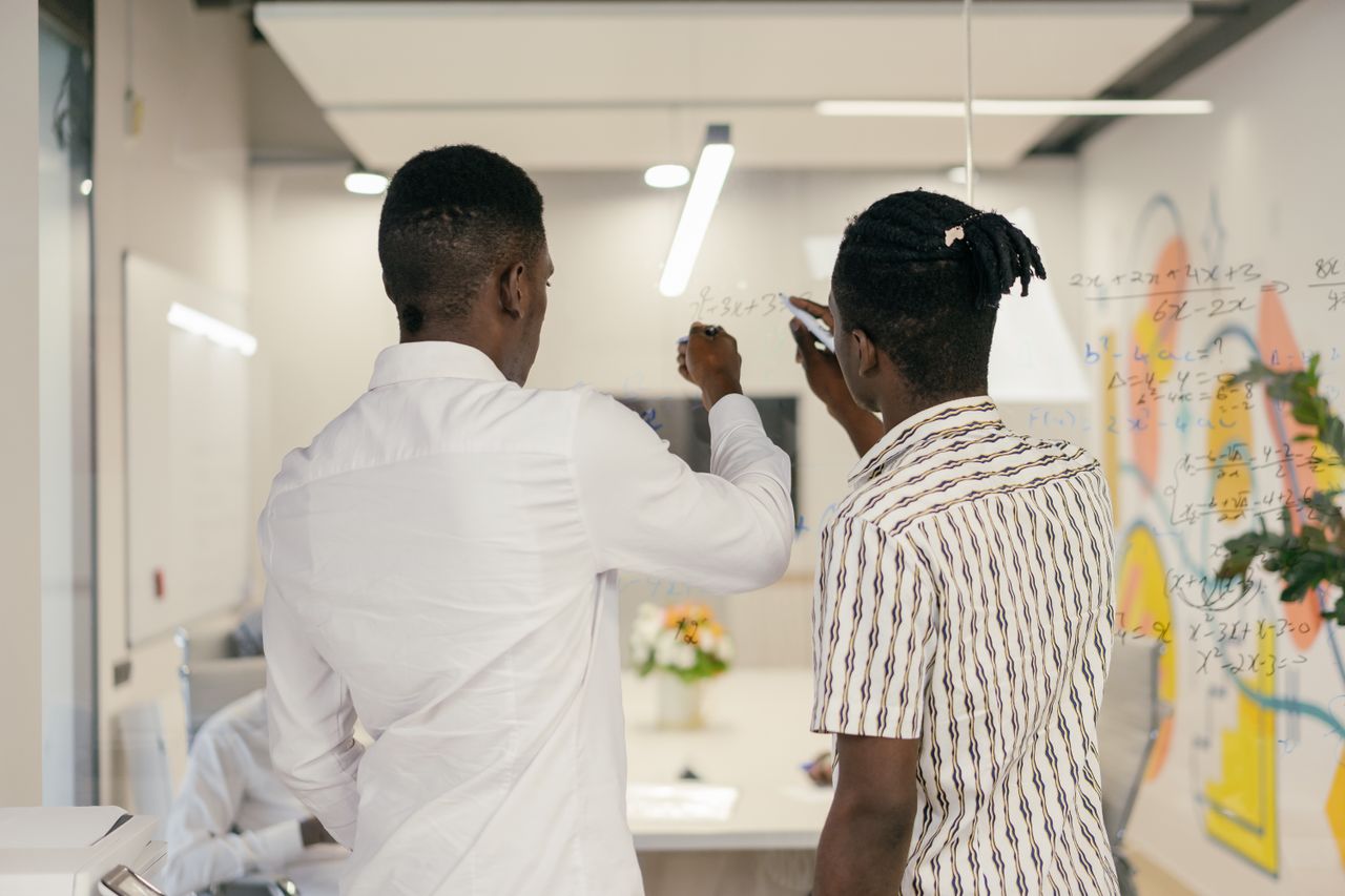 Two men collaborating and writing on a glass wall in a modern office environment, demonstrating teamwork.